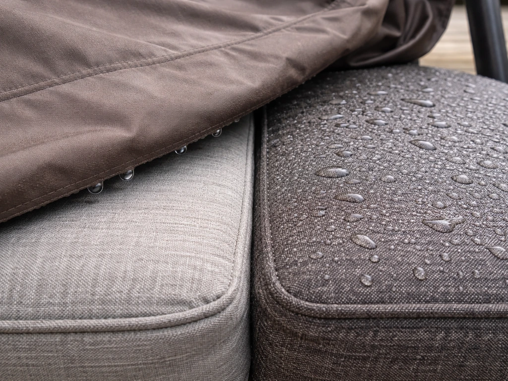 Close-up of patio swing cushion fabric, half dry under cover and half wet from rain outside.