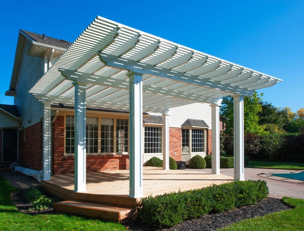 A white pergola-style patio cover installed over a backyard patio next to a house.