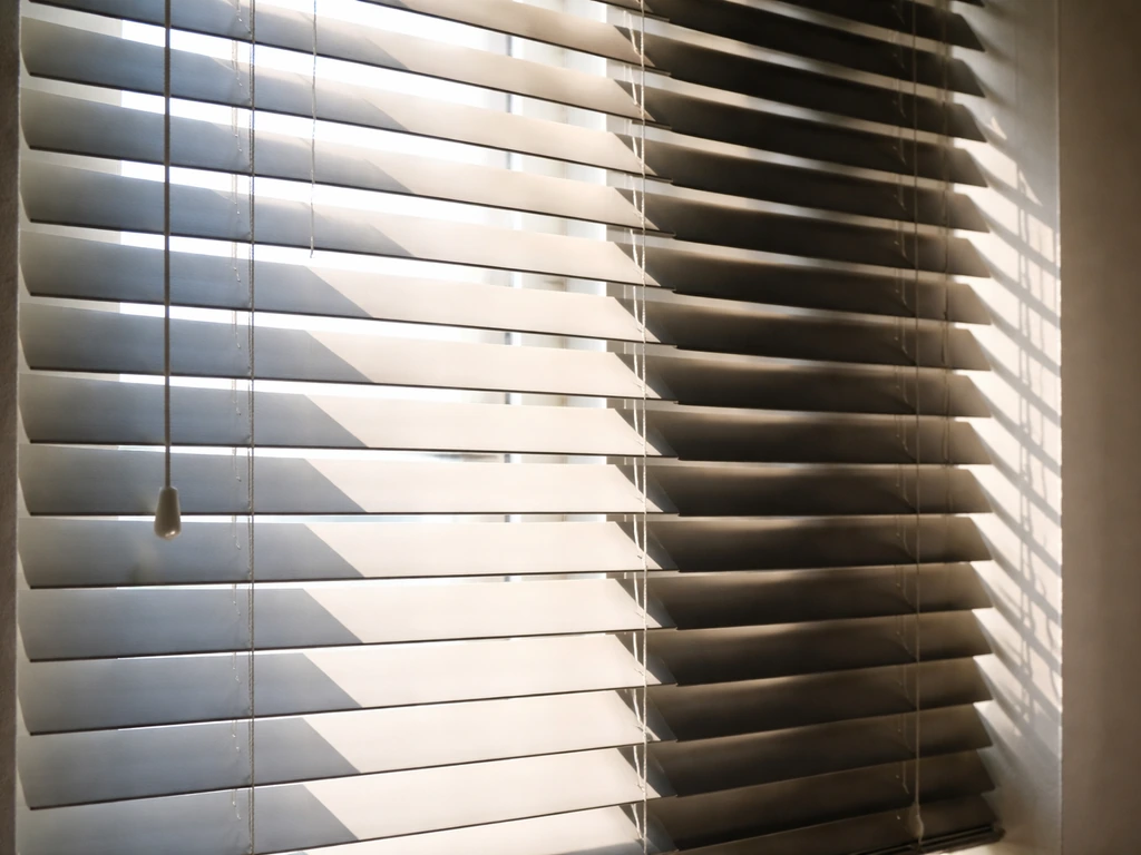 Close-up of adjustable slatted blinds with different angled openings creating alternating light and shadow bands.